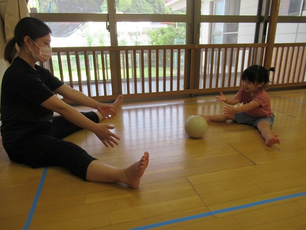 向かい合ってボールを転がす、保育者と、女の子
