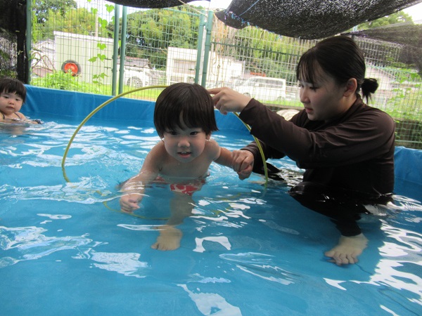 保育者と手を繋ぎながらフラフープをくぐる男の子