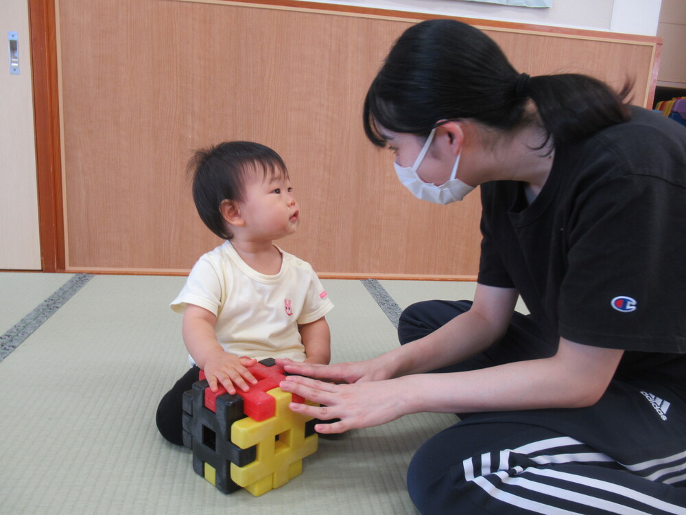 太鼓のようにして遊ぶ女の子と保育者