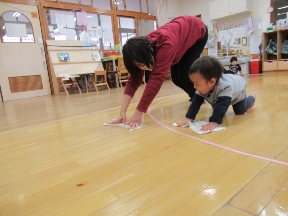 保育者と一緒に雑巾がけをする男の子