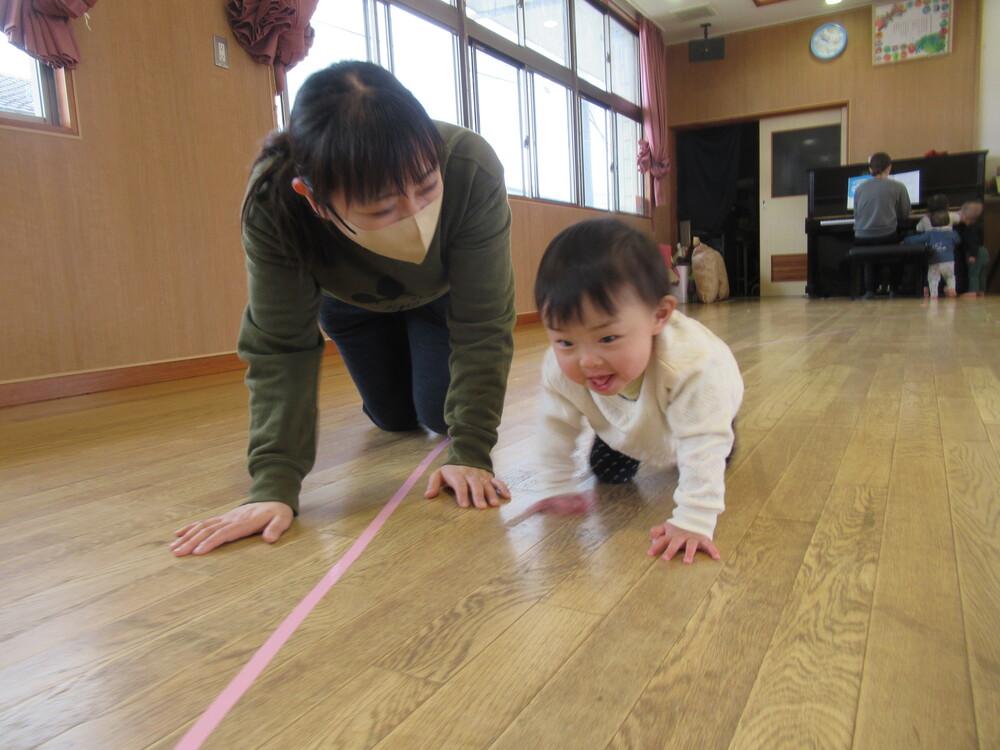 女の子が保育者と一緒にハイハイをしている